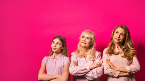 Three different generations from women standing against a pink background