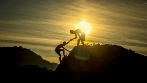 Two children help each other climb a rock in the sunrise