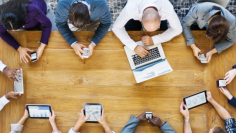 A group of people around a table all looking at different devices